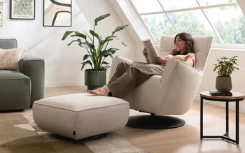 Frau sitzt gemütlich auf einem Sessel und liest einen Möbelkatalog